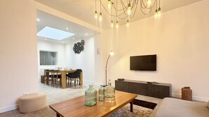 Un salon moderne avec une table basse en bois, un canapé, un téléviseur fixé au mur et, au fond, un coin repas.