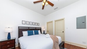 A bedroom with a bed, nightstands, a ceiling fan, framed pictures, and doors.