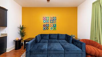 A living room with a blue sectional sofa, a small table, and a colorful wall art piece.