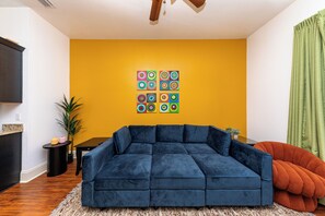 Ein Wohnzimmer mit einem blauen Modulsessel, einem kleinen Tisch und einem farbenfrohen Wandbild.