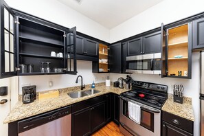 A modern kitchen with black cabinets, granite countertops, stainless steel appliances, and open shelving.