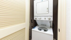 Une petite buanderie blanche, équipée d’un lave-linge et d’un sèche-linge intégrés, d’un panneau de commande et d’un tuyau d’évacuation.
