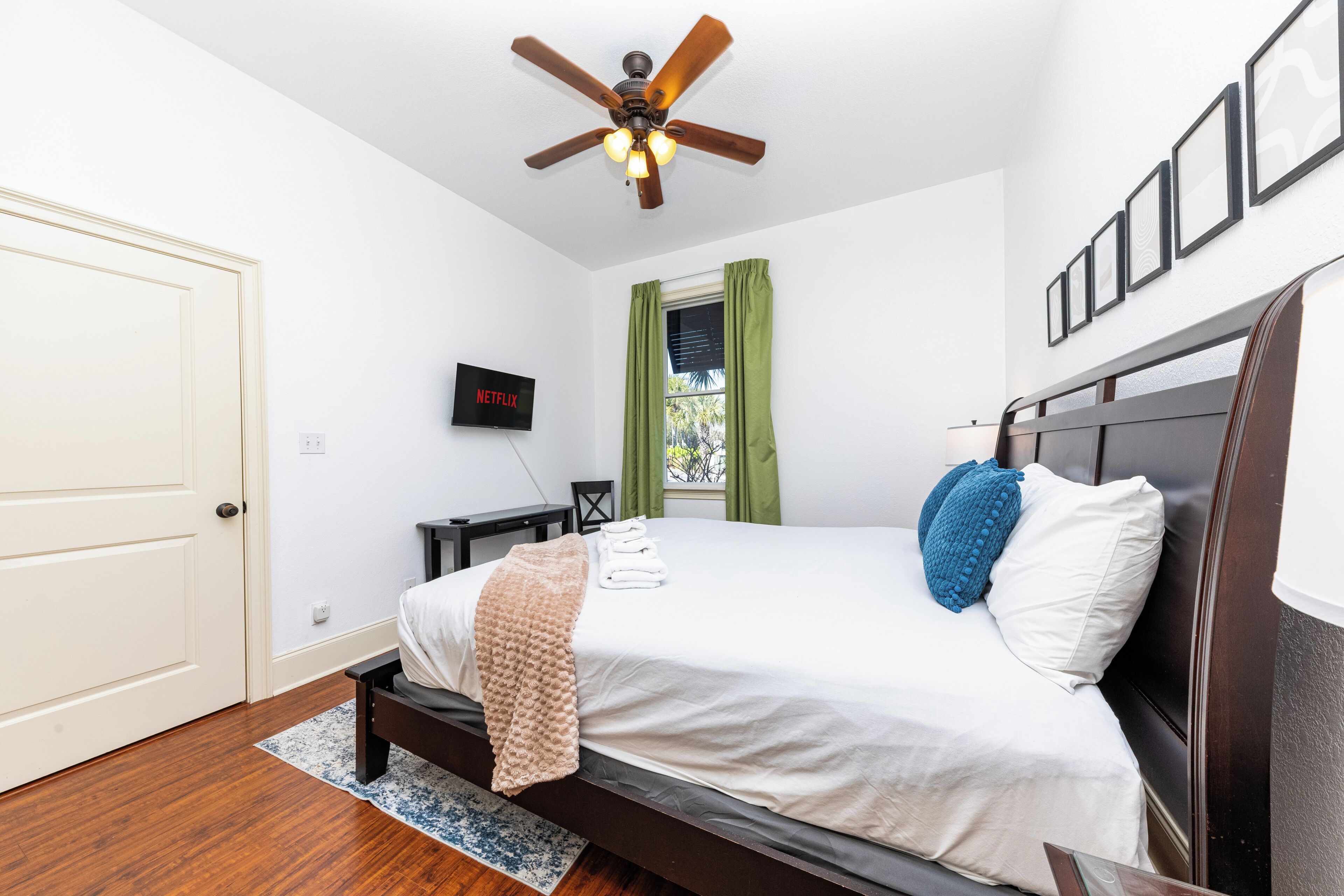 Un dormitorio con cama, ventilador de techo, televisión y ventana con cortinas.