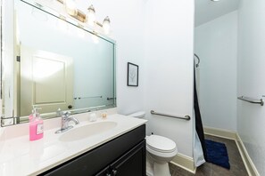 Een badkamer met een wit wastafelmeubel, een spiegel, een toilet en een douchehoek.