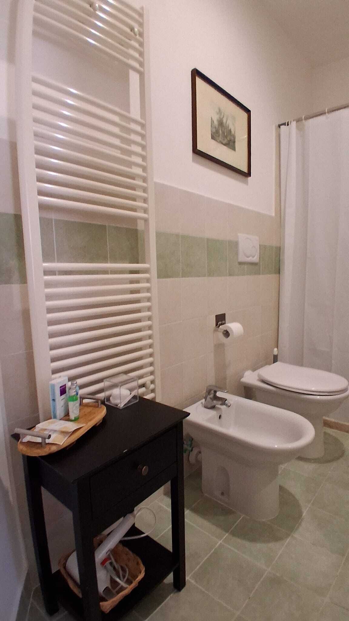 Un baño con bañera, dos inodoros, un lavabo, tocador con espejo y un cuadro en la pared.