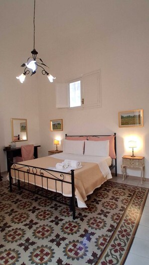 Ein Schlafzimmer mit einem Bett, Nachttischen, einer Pendelleuchte, einem Fenster und einem gemusterten Teppich.