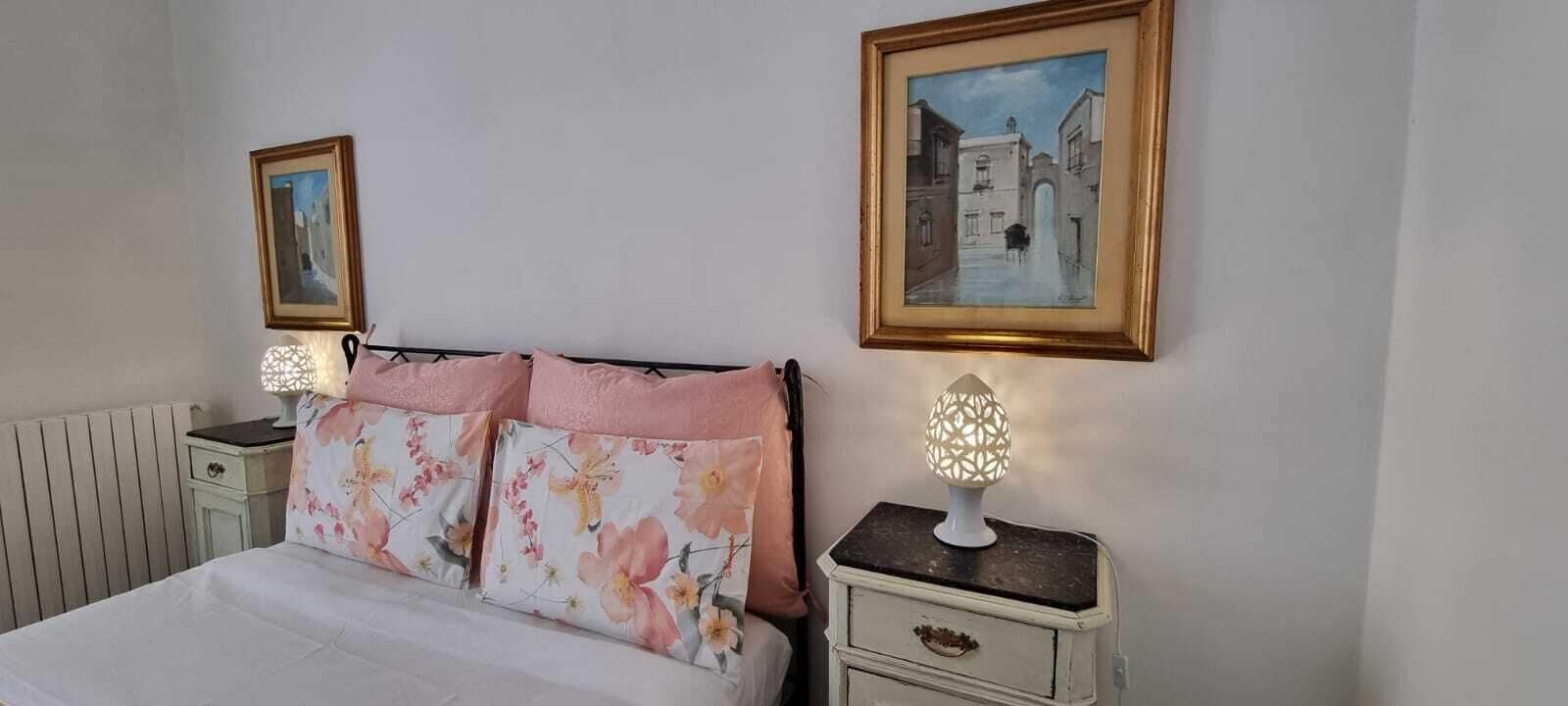 A bedroom with a bed, two nightstands, a radiator, and two framed pictures on the wall.