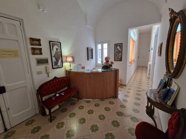 A reception area with a wooden desk, a red bench, and a mirror on the wall. - BnB 900 (Lecce)