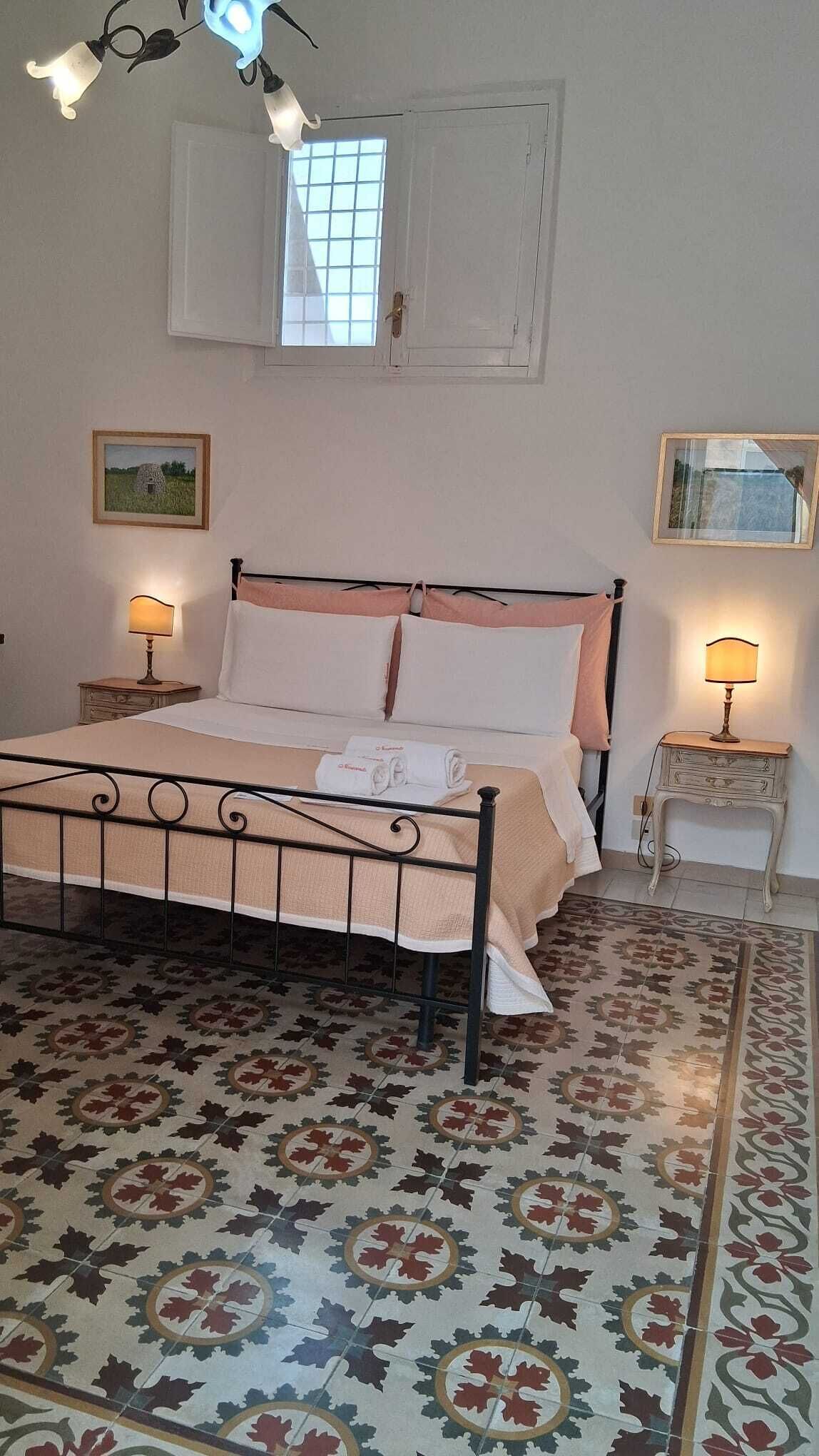 A bedroom with a bed, two bedside tables with lamps, a window with a view, and a patterned floor.