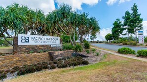 En skylt för Pacific Harbour Golf & Country Club, med en vacker trädgård och en väg i bakgrunden.