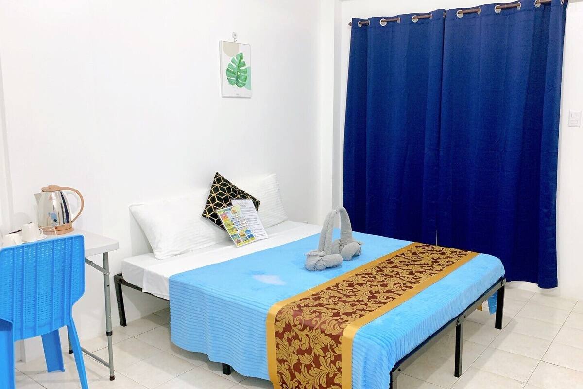 Ein Hotelzimmer mit einem Bett, einem Tisch mit Wasserkocher, einem Stuhl und einem blauen Vorhang.