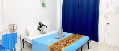 Habitación de hotel con cama, una mesa con hervidor, una silla y una cortina azul.