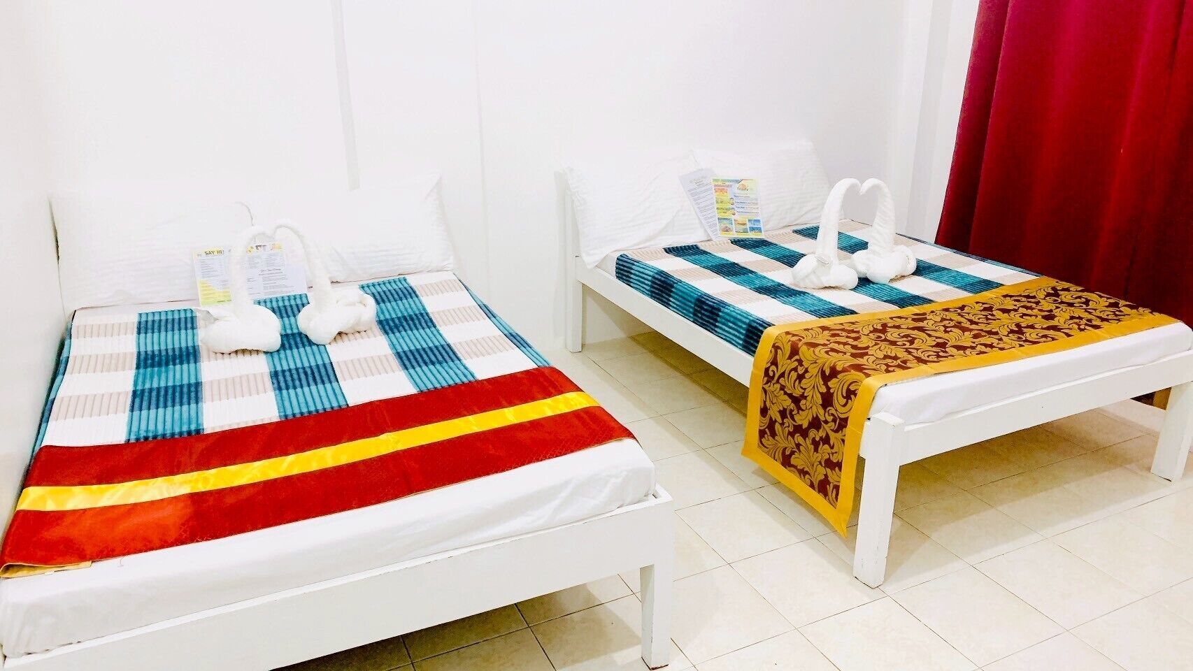 Two single beds with white frames and blue and red striped bedding. Each bed has a white pillow and a white towel.