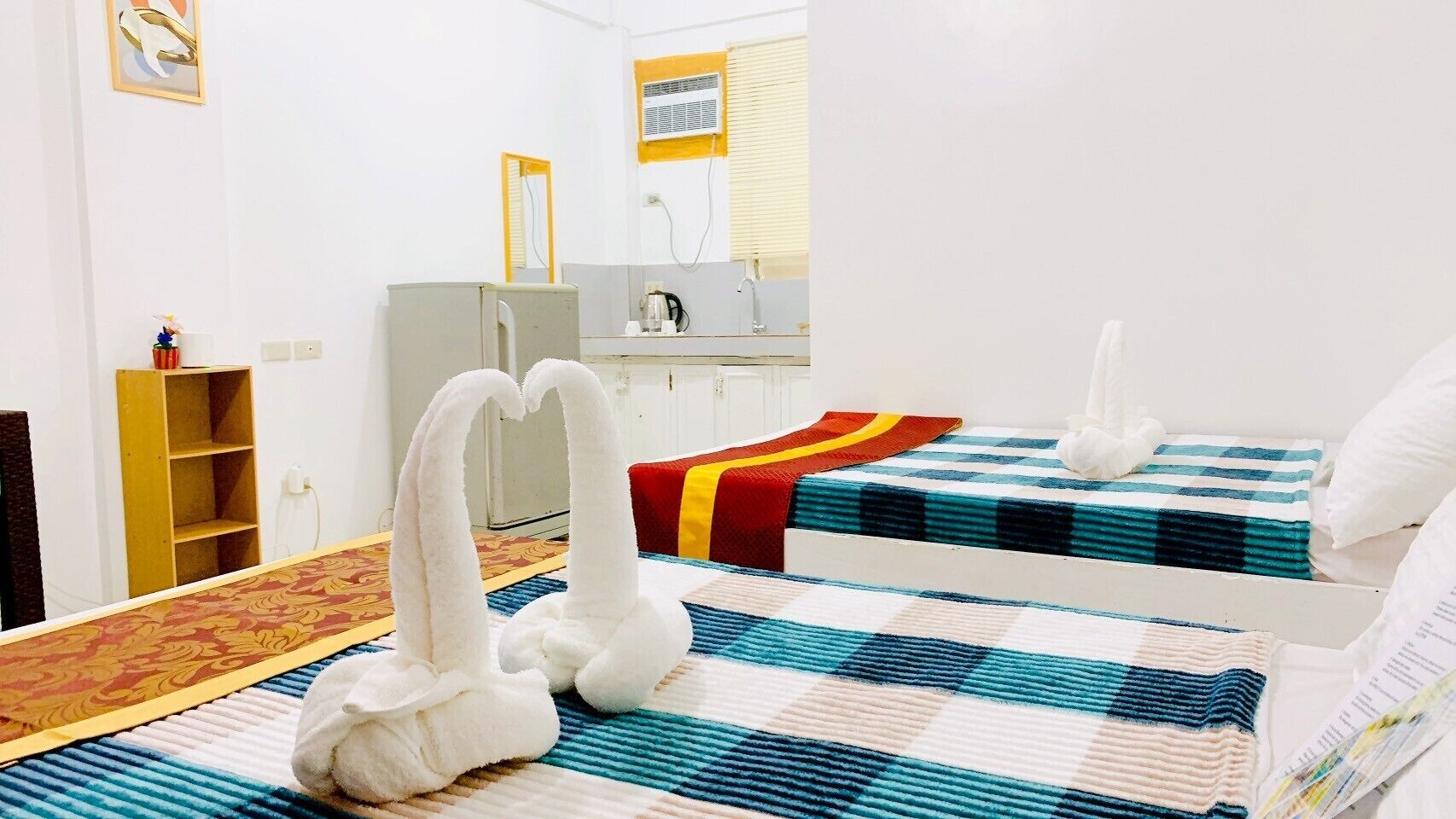 Hotellihuone, jossa on kaksi sänkyä, pieni keittokomero, peili ja puinen hylly.