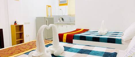 A hotel room with two beds, a small kitchenette, a mirror, and a wooden shelf.