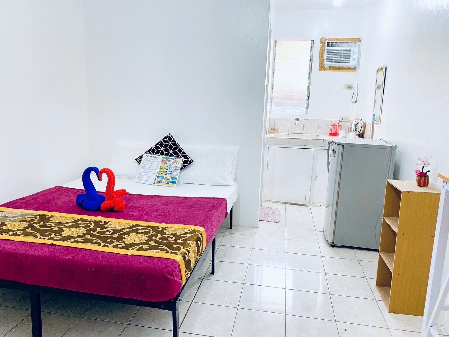 A small, clean room with a bed, a desk, and a kitchenette.