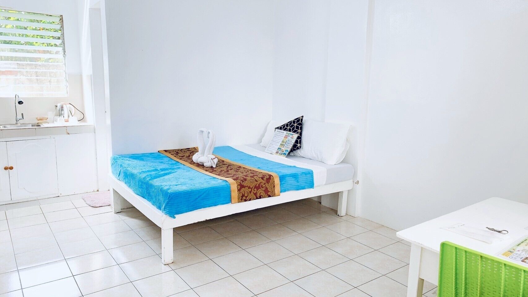 A small, clean room with a bed, a white table, and a window with blinds.