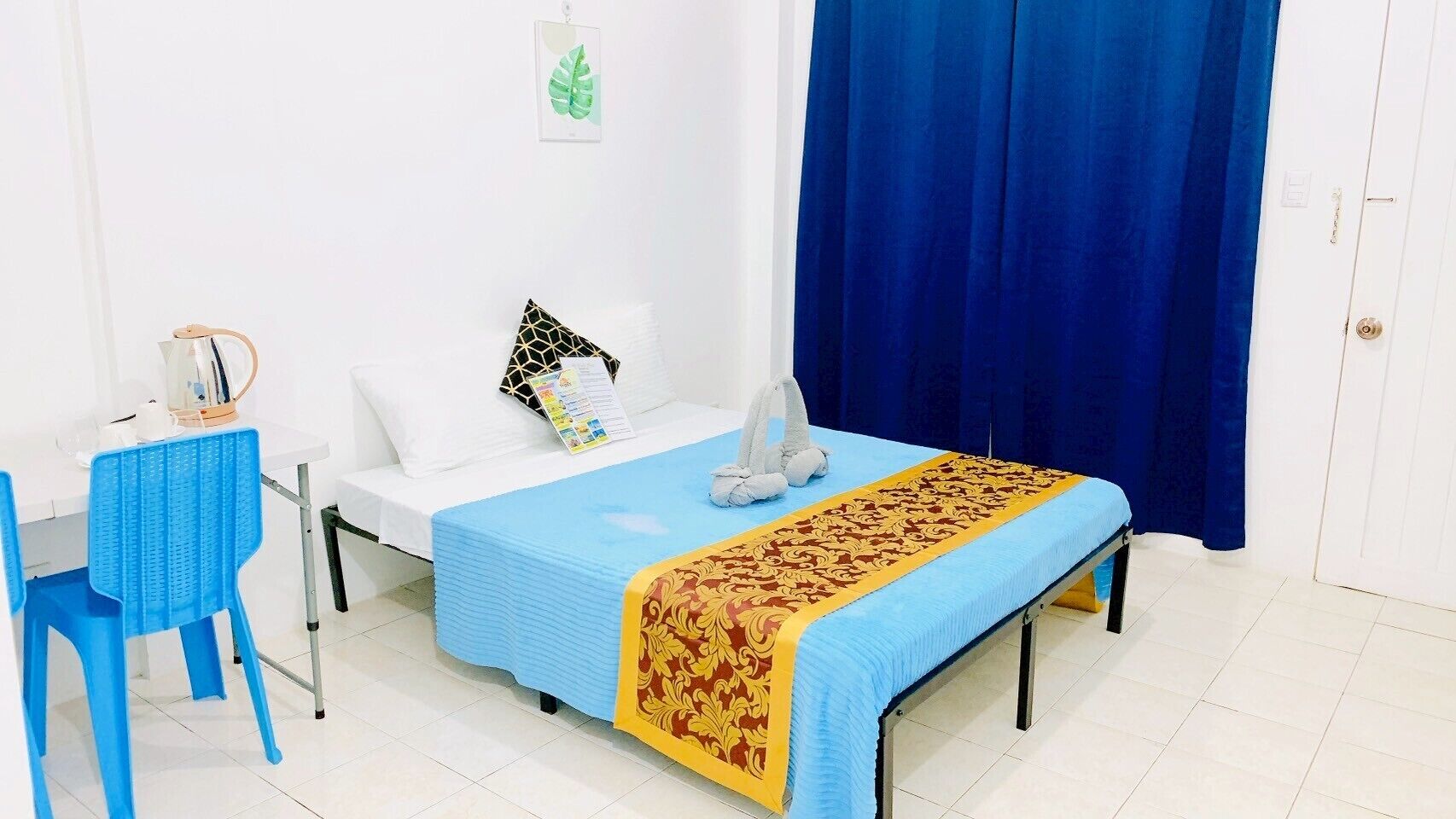 Una habitación con cama, escritorio, silla y ventana con cortinas azules.