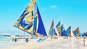 A beach with multiple sailboats docked, featuring colorful sails with various designs. - Glo's Space Boracay Dmall (Boracay Island)