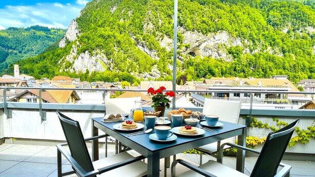 Mesa al aire libre con alimentos para el desayuno, con vistas a un paisaje montañoso.