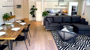 Un salón moderno con un sofá gris oscuro, una mesa de comedor de madera para cuatro comensales y una alfombra con diseño blanco y negro.