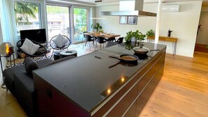 Cocina moderna con isla central, comedor con sillas y un televisor.
