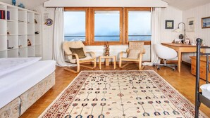 Una habitación acogedora con un ventanal grande, muebles de madera, una cama blanca y una alfombra estampada.
