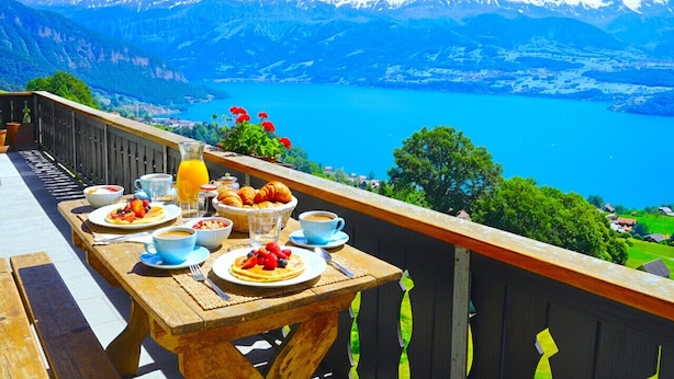 Una mesa de madera dispuesta con alimentos para el desayuno y una vista panorámica de montañas.