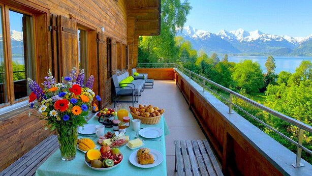 A wooden deck with a breakfast setup overlooking a lake and mountains.