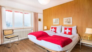 A hotel room with a large bed, a chair, a window, and wooden paneling. - Concierge, Lake Thun/Alps Scenic Views by SwissHut (Sigriswil)