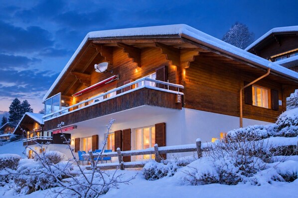 Een houten chalet met een balkon, omgeven door besneeuwde begroeiing.