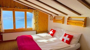 Un dormitorio con cama, ventana con vistas, vigas de madera y una manta roja.