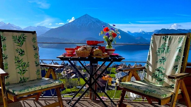 Una mesa con una cesta de pan, un florero y dos sillas, con vistas a un lago y montañas.