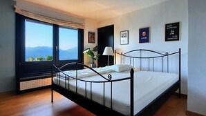 A modern bedroom with a metal bed frame, a large window with a view of mountains, and three motivational posters on the wall.