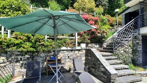 An outdoor patio with a stone wall, a metal staircase, and a green umbrella.