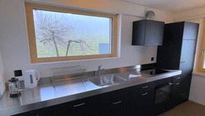 Una cocina moderna con un amplio ventanal, electrodomésticos de acero inoxidable y armarios oscuros.
