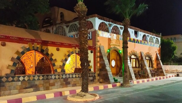 A building with arched windows and a decorative facade, featuring a palm tree in the foreground. - Tuya hotel (Abu Simbel)