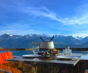 A table with a pot, glasses, and a jar, overlooking a mountain range. - Concierge, Lake Thun/Alps Scenic Views by SwissHut (Merligen)