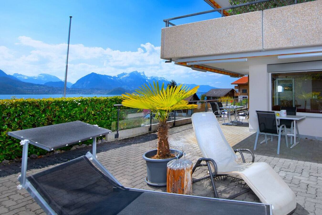 Een terras met loungezetels, een potplant en uitzicht op bergen en water.