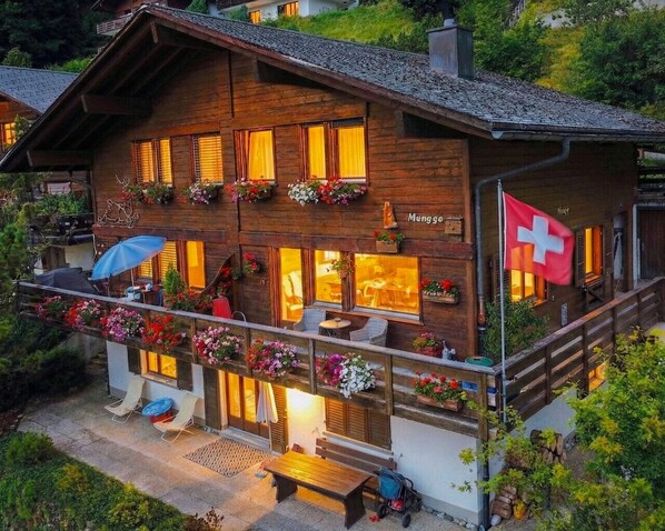 A wooden chalet with a balcony, outdoor seating, and a Swiss flag.
