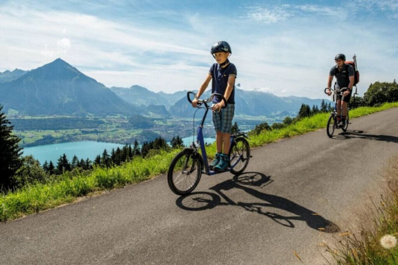 Two cyclists on a paved road with a scenic mountain view in the background.
