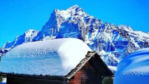 A snow-covered wooden cabin with a mountain backdrop.