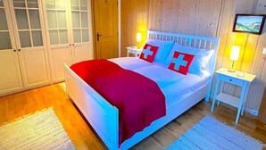A bedroom with a bed, wooden walls, a door, and a nightstand with a lamp.