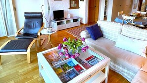 A modern living room with a sofa, a chair, a coffee table with magazines, a TV, and a lamp.