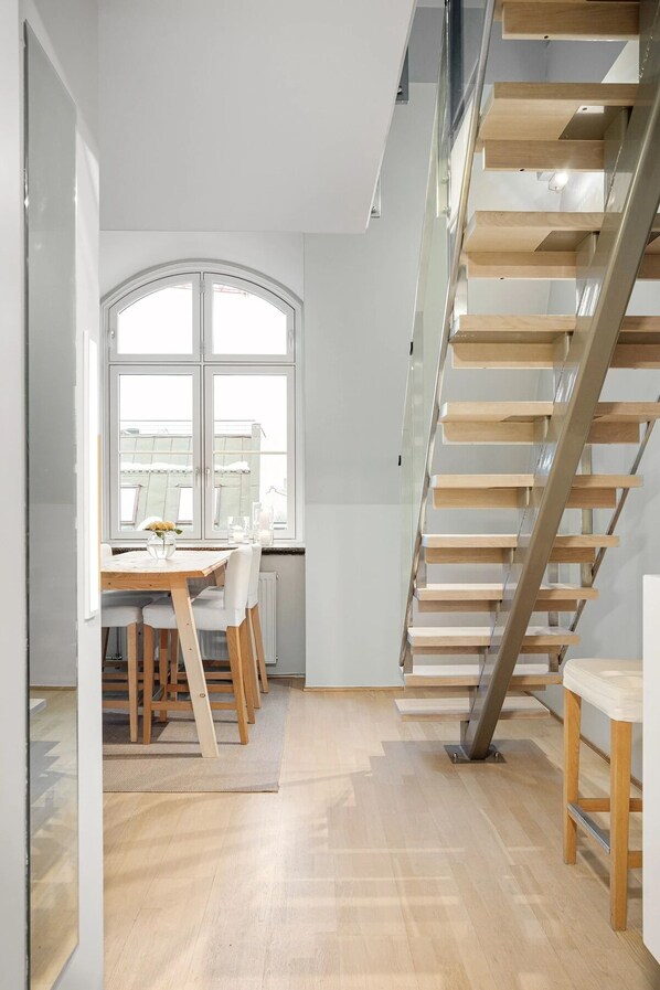 A modern interior with a wooden staircase, a dining area with a table and chairs, and large windows.