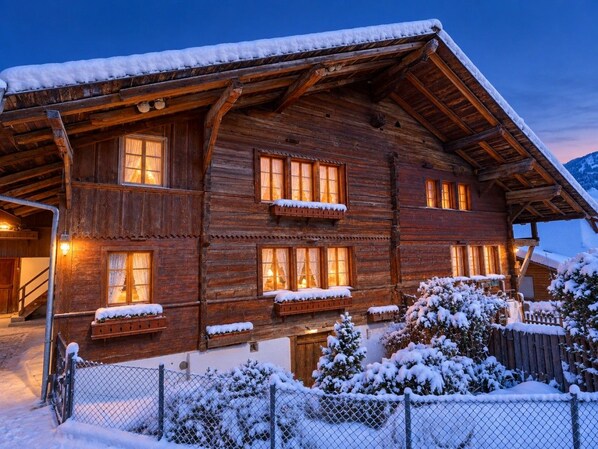 Un chalet en bois doté de nombreuses fenêtres, d’un porche abrité et entouré d’un paysage enneigé.