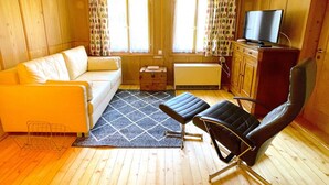 A cozy living room with a sofa, a black leather chair, a small wooden cabinet, and a television on a stand.