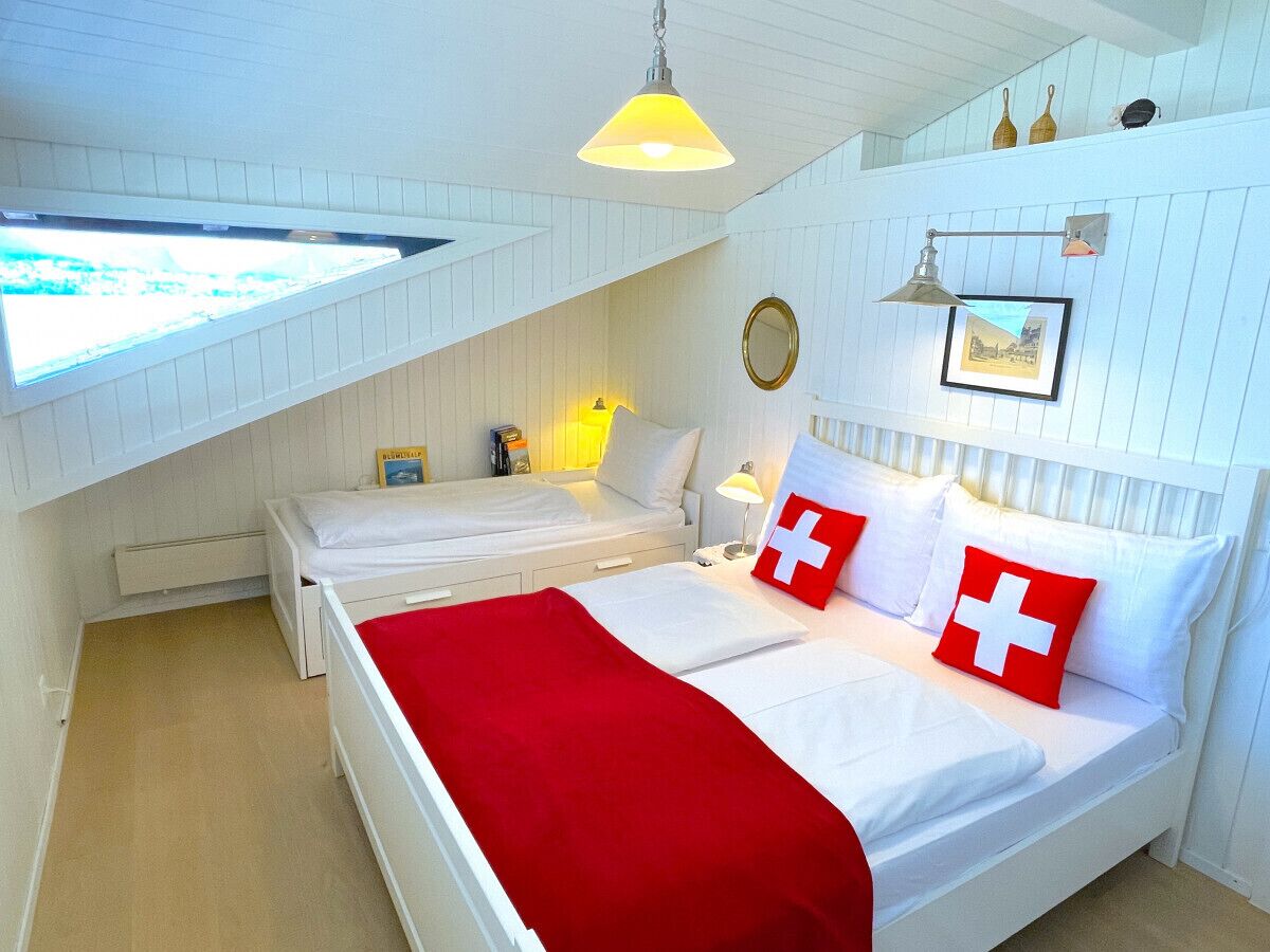 A bedroom with two beds, a red blanket, and a Swiss flag pillow.