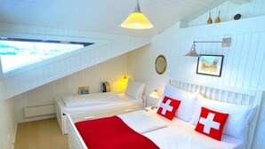 Une chambre avec deux lits, une couverture rouge et un coussin orné du drapeau suisse.