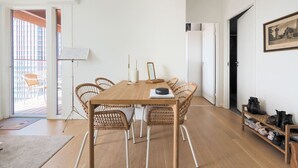 Tilava huone, jossa on puinen ruokapöytä, jonka ympärillä on punottuja tuoleja, lattiavalaisin ja seinällä oleva kehystetty taulu.